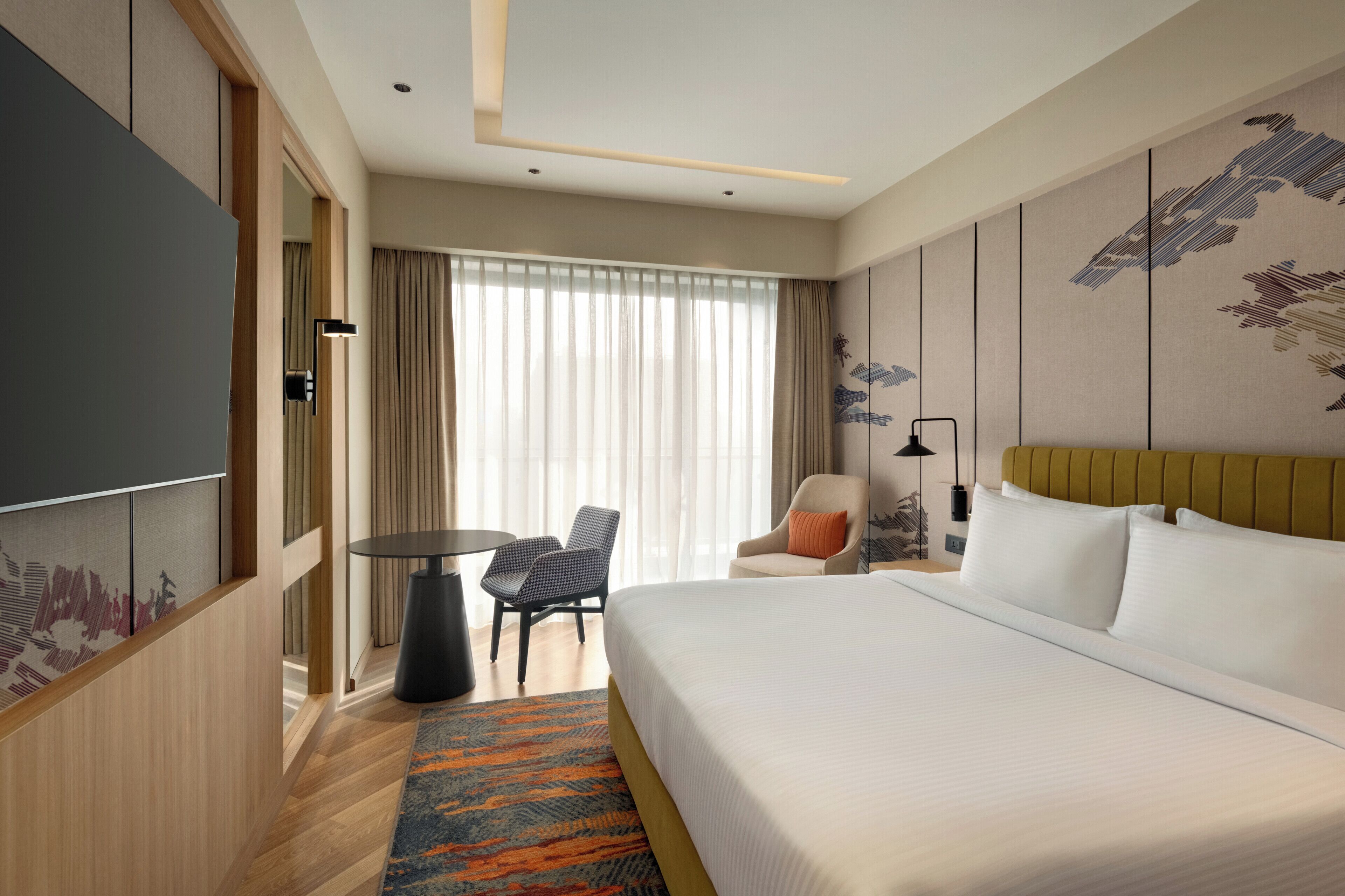 A hotel room with a large bed, a desk, a chair, and a TV.