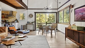 A spacious living room with a high ceiling, a dining area with wicker chairs, a leather sofa, and a wooden coffee table. - TreeLicious | Jacuzzi, Cozy Chalet close to Slopes (Big Bear Lake)