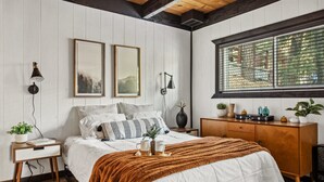 A bedroom with a bed, bedside tables, a dresser, and a window with a view. - TreeLicious | Jacuzzi, Cozy Chalet close to Slopes (Big Bear Lake)
