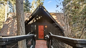 A wooden cabin with a red door, a brick pathway leading to it, and a metal railing on the walkway. - TreeLicious | Jacuzzi, Cozy Chalet close to Slopes (Big Bear Lake)