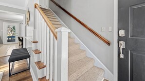 Una escalera con barandillas de madera y peldaños alfombrados en color beige, que conduce a una puerta oscura.