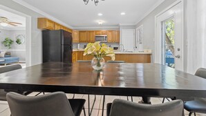 Una cocina moderna con armarios de madera, un refrigerador negro y una zona de comedor con una mesa grande y sillas.