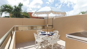 A balcony with a white table and chairs, a white umbrella, and a small white refrigerator. - 27 Ely House (Cancún)