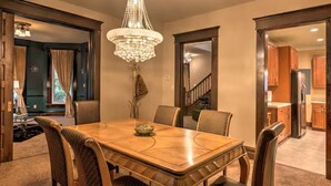 A dining room with a wooden table and chairs, a chandelier, and a view of the kitchen and staircase.