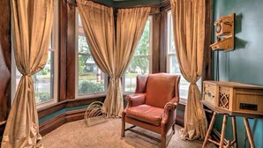 A room with a leather armchair, a wooden radio, and large windows with curtains.