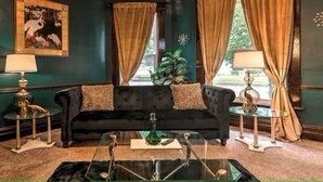 A dark green-walled room with a black sofa, two side tables, and a glass coffee table.