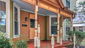 A wooden house with a porch, a number "1210" on the door, and steps leading up to the entrance.