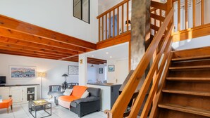 Amplia sala de estar con escalera de madera, un sofá, una mesa de comedor y zona de cocina.