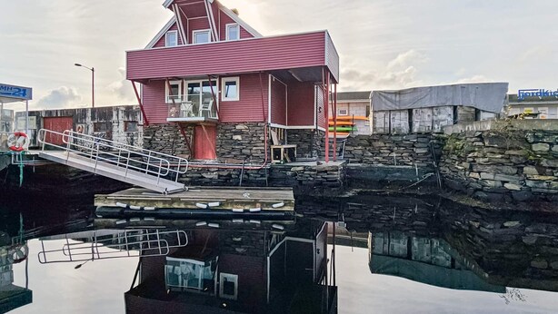 Un edificio rosso con un balcone, un muro di pietra e un molo.