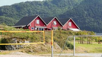 A row of red houses with dark roofs, set against a backdrop of a forested hillside.