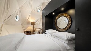 A modern bedroom with a large bed, a round mirror, and a unique tent-like ceiling structure. - Domes at Catskills a lakefront glamping adventure for adults (Swan Lake)