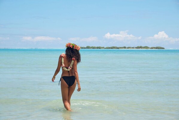 A person walking in shallow water with a clear view of the ocean and distant land.