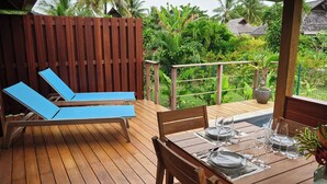A wooden deck with a table set for dining, blue lounge chairs, and a wooden fence. - Single Tropical Pool Villa (MOOREA MAIAO)