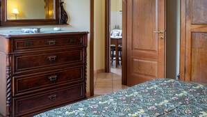 A bedroom with a wooden dresser, a bed with a floral bedspread, and a mirror above the dresser.