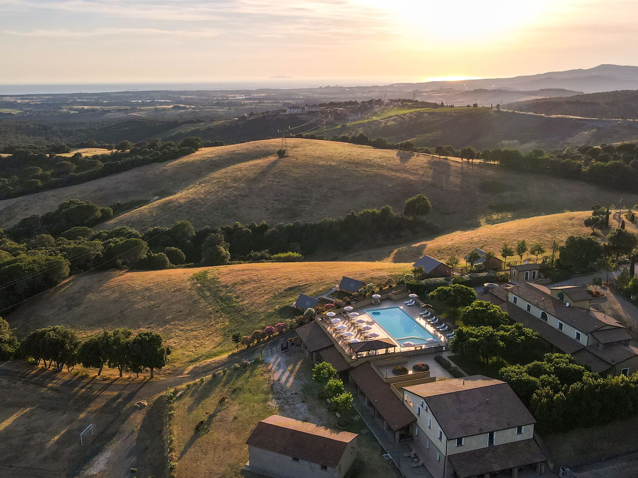 An aerial view of a resort with a swimming pool, villas, and rolling hills in the background.