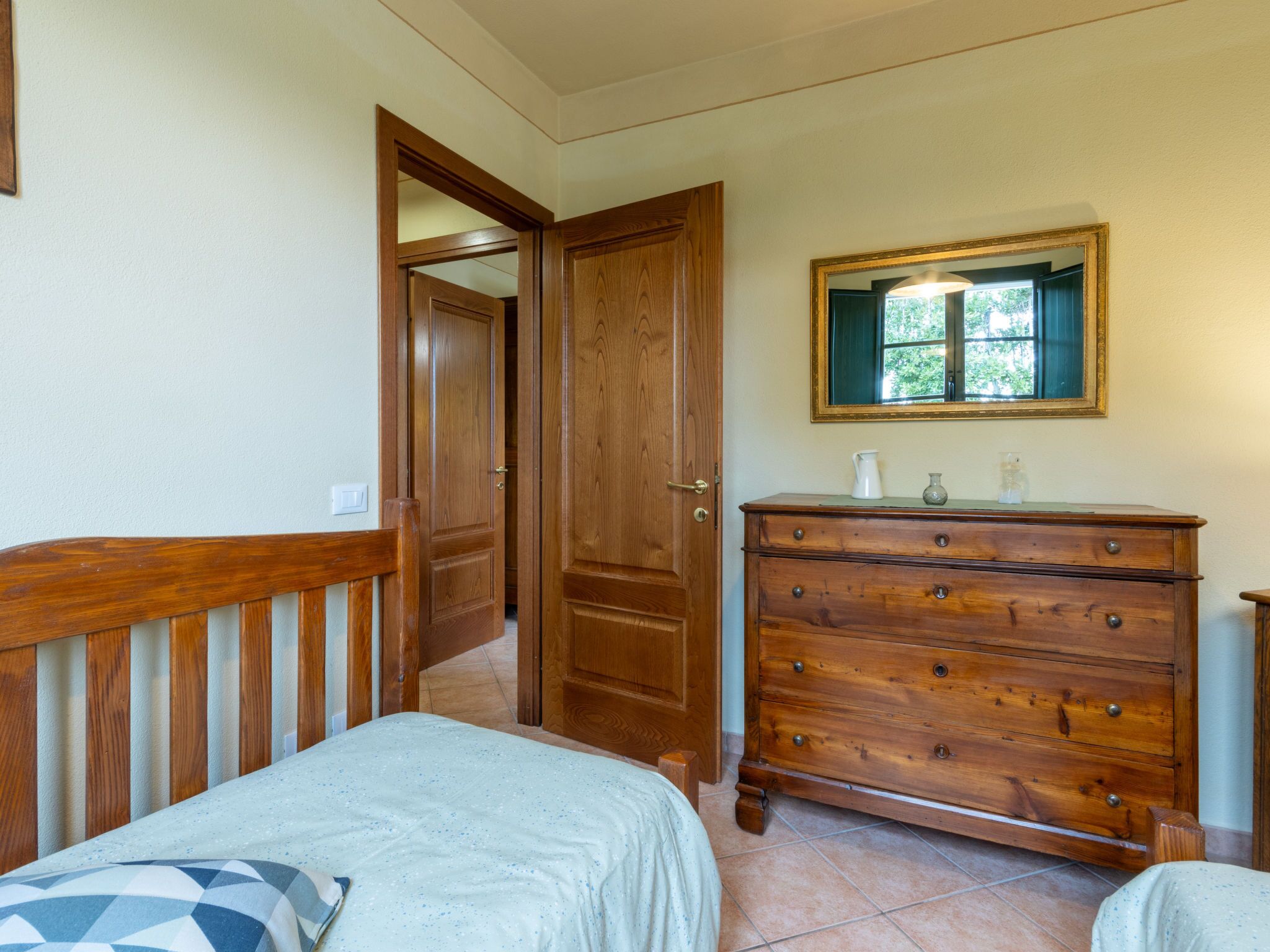 Une chambre à coucher avec une commode en bois, un lit recouvert d’une couvre-lit à motifs et un miroir au mur.