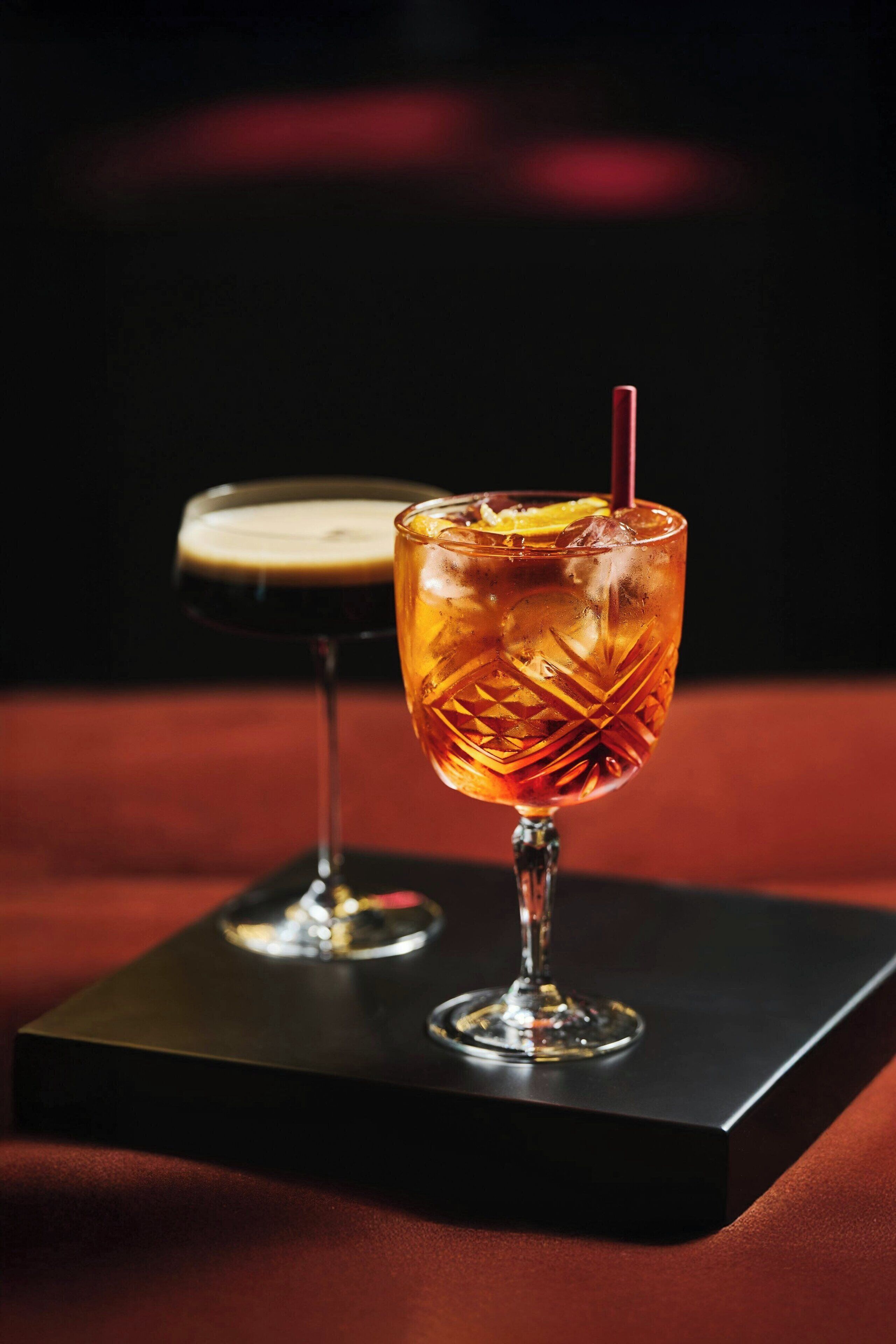 A glass of amber-colored beverage with a straw, placed on a black rectangular base.