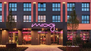 Un edificio moderno con un letrero de neón que dice "moosy" y una entrada bien iluminada.