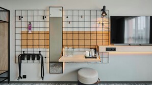 A modern hotel room with a kitchen area, a seating area with a table and chairs, a TV mounted on the wall, and a small stool. - Moxy Warsaw City (Warsaw)