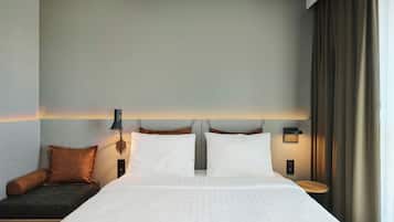 A hotel room with a large bed, two bedside tables, a wall-mounted lamp, and a window with curtains.