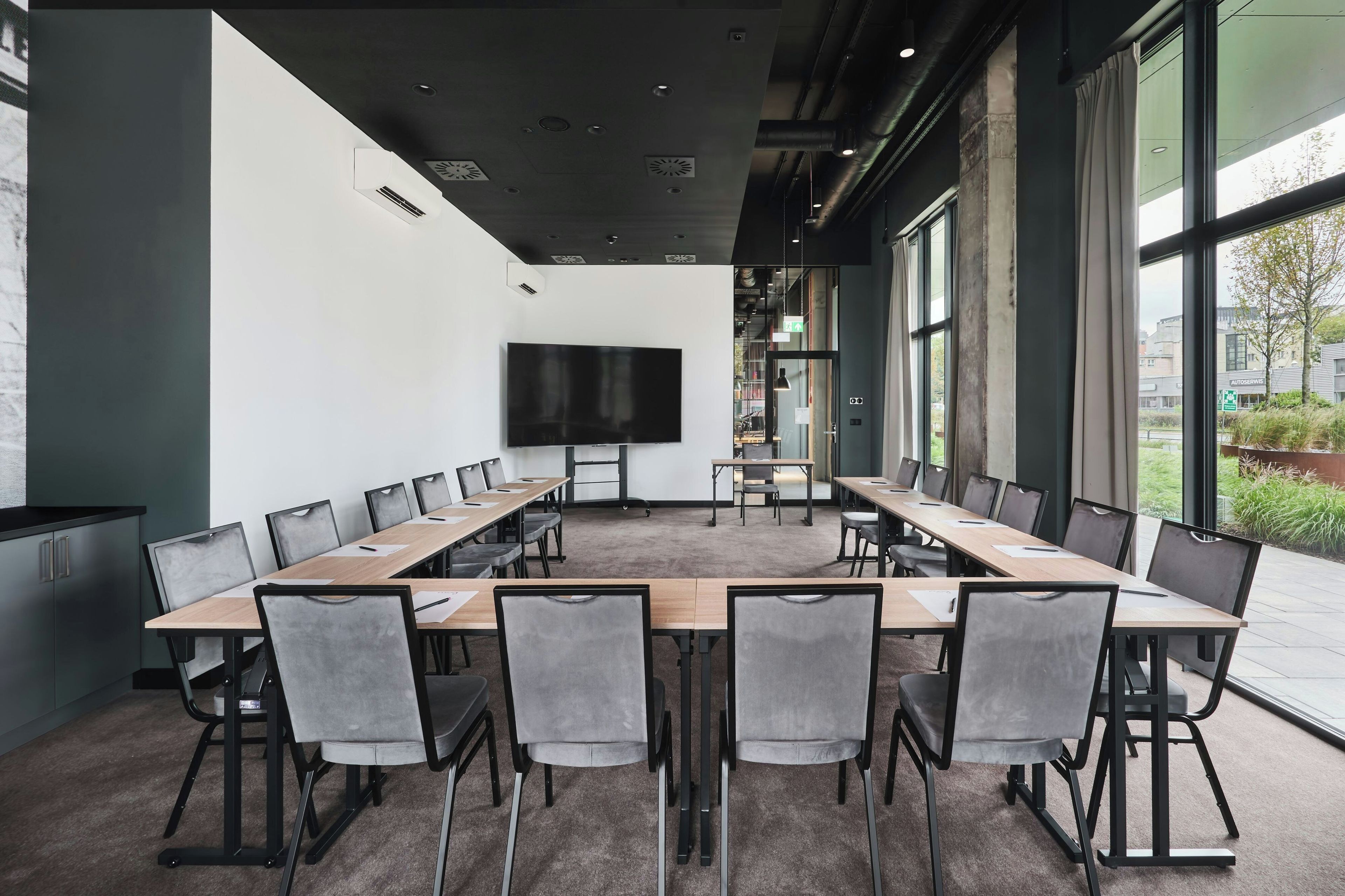 Un salón de conferencias con una gran mesa, sillas, un televisor de pantalla plana y ventanas amplias.