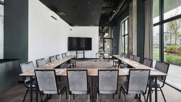 Un salón de conferencias con una gran mesa, sillas, un televisor de pantalla plana y ventanas amplias.