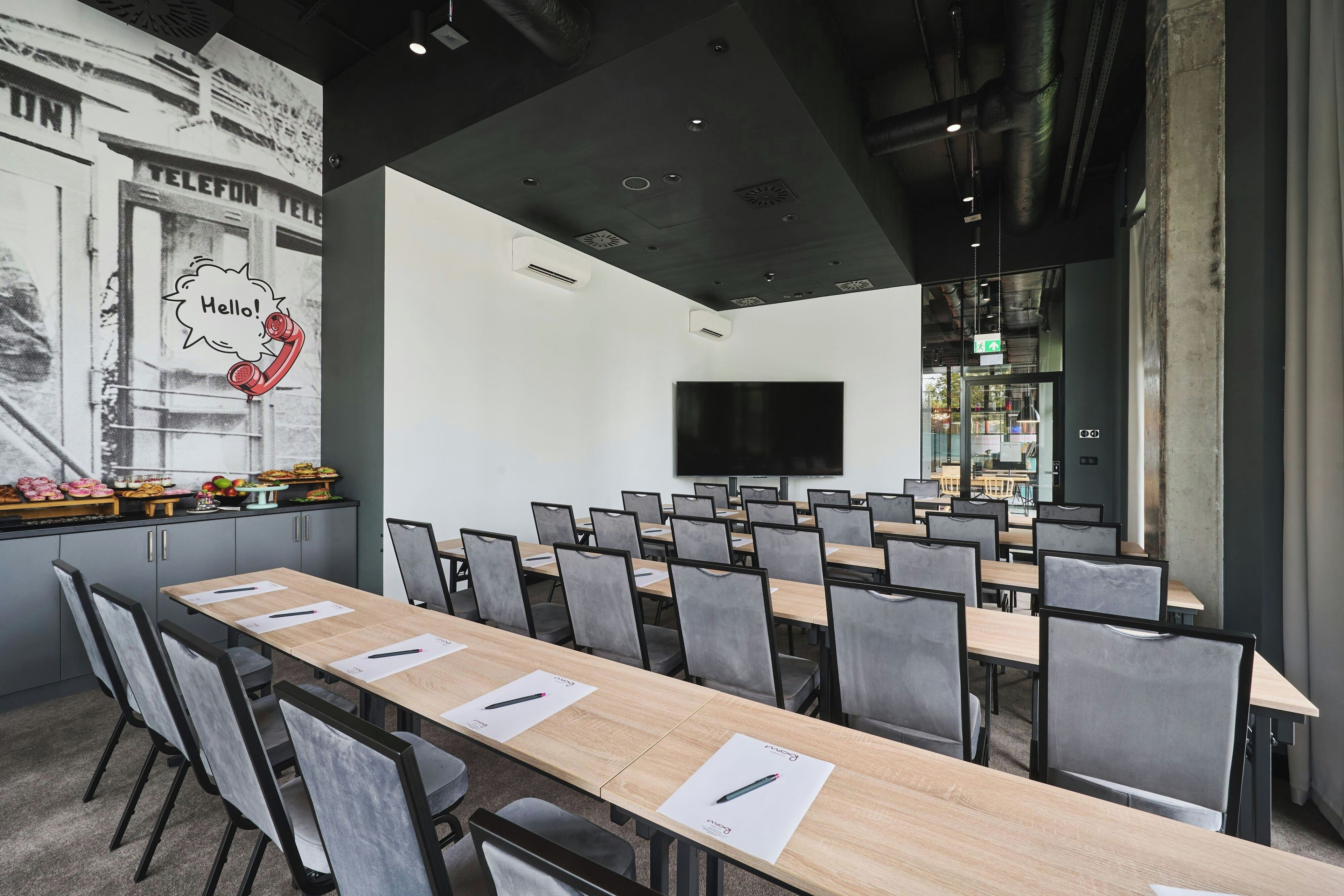 Une salle de conférence équipée de plusieurs tables et chaises, d’un grand écran et d’un mur orné d’une illustration représentant un téléphone d’époque.