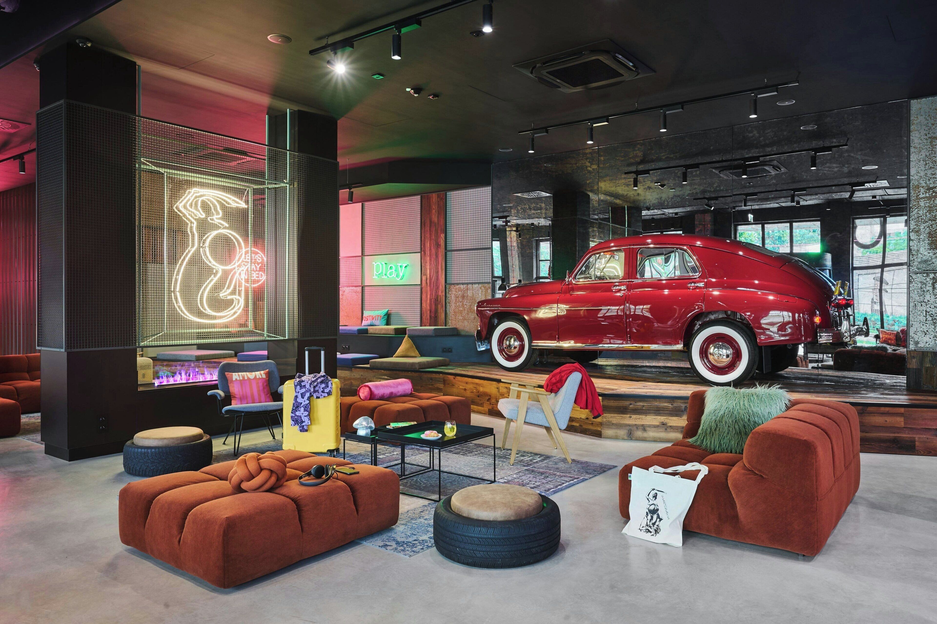 A modern lounge area with a vintage car display, comfortable seating, and a neon sign.