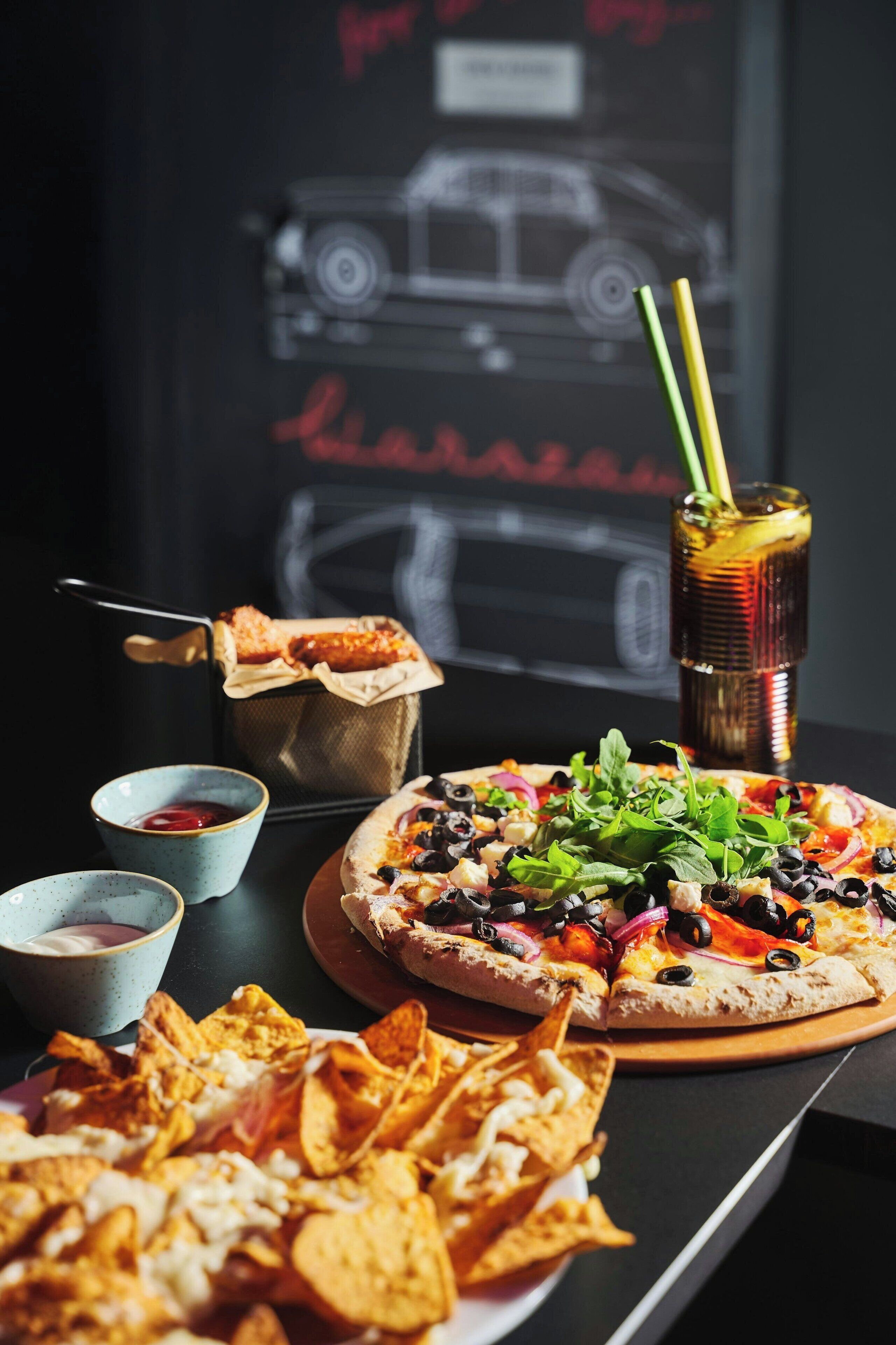 Una pizza con diversi condimenti, una bevanda con una cannuccia e una ciotola di patatine su un tavolo.