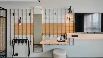 A modern hotel room with a large mirror, a flat-screen TV, a wooden table with a tray, and a seating area.