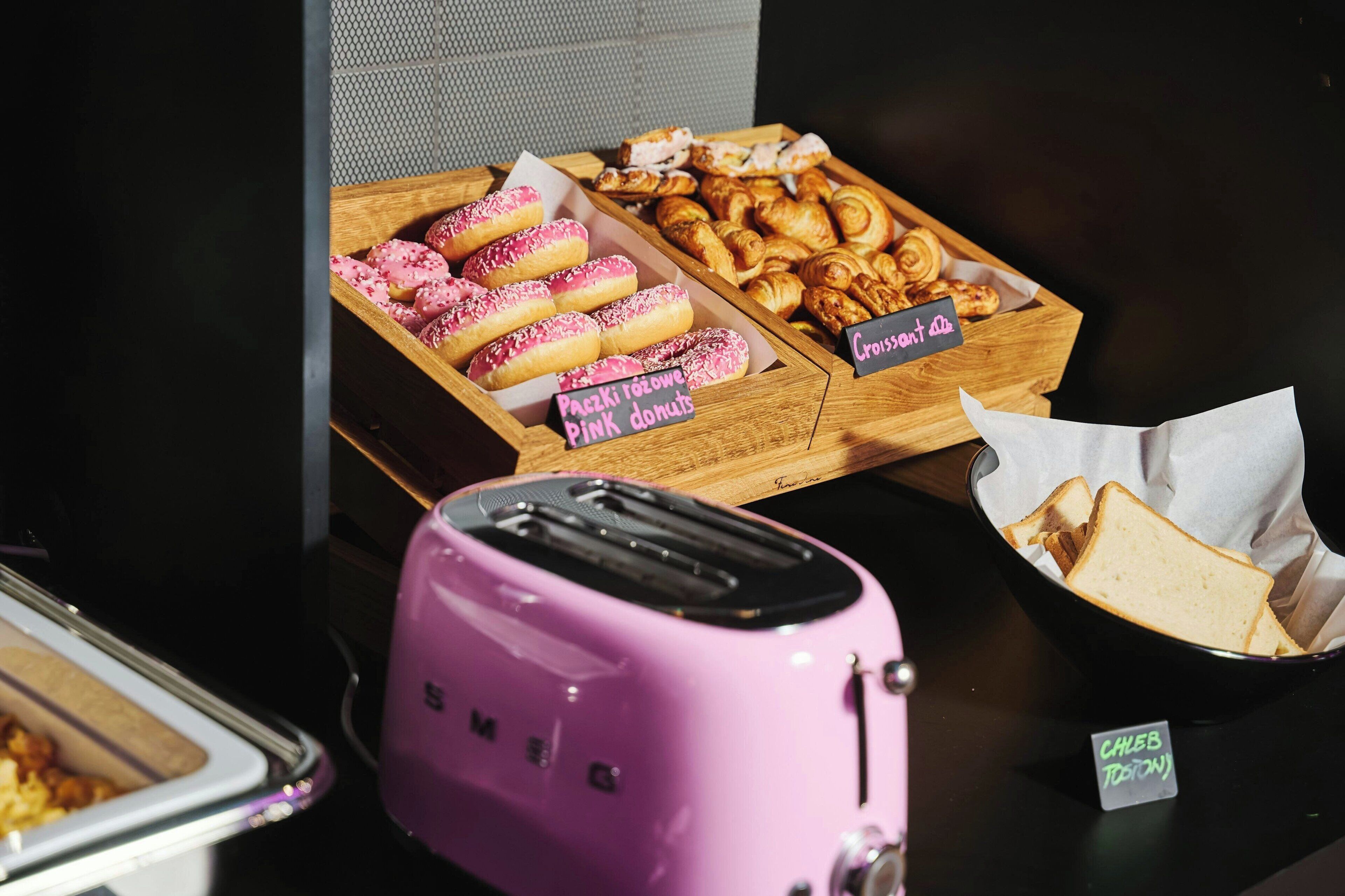 Een ontbijtbuffet met roze donuts, croissants en brood.