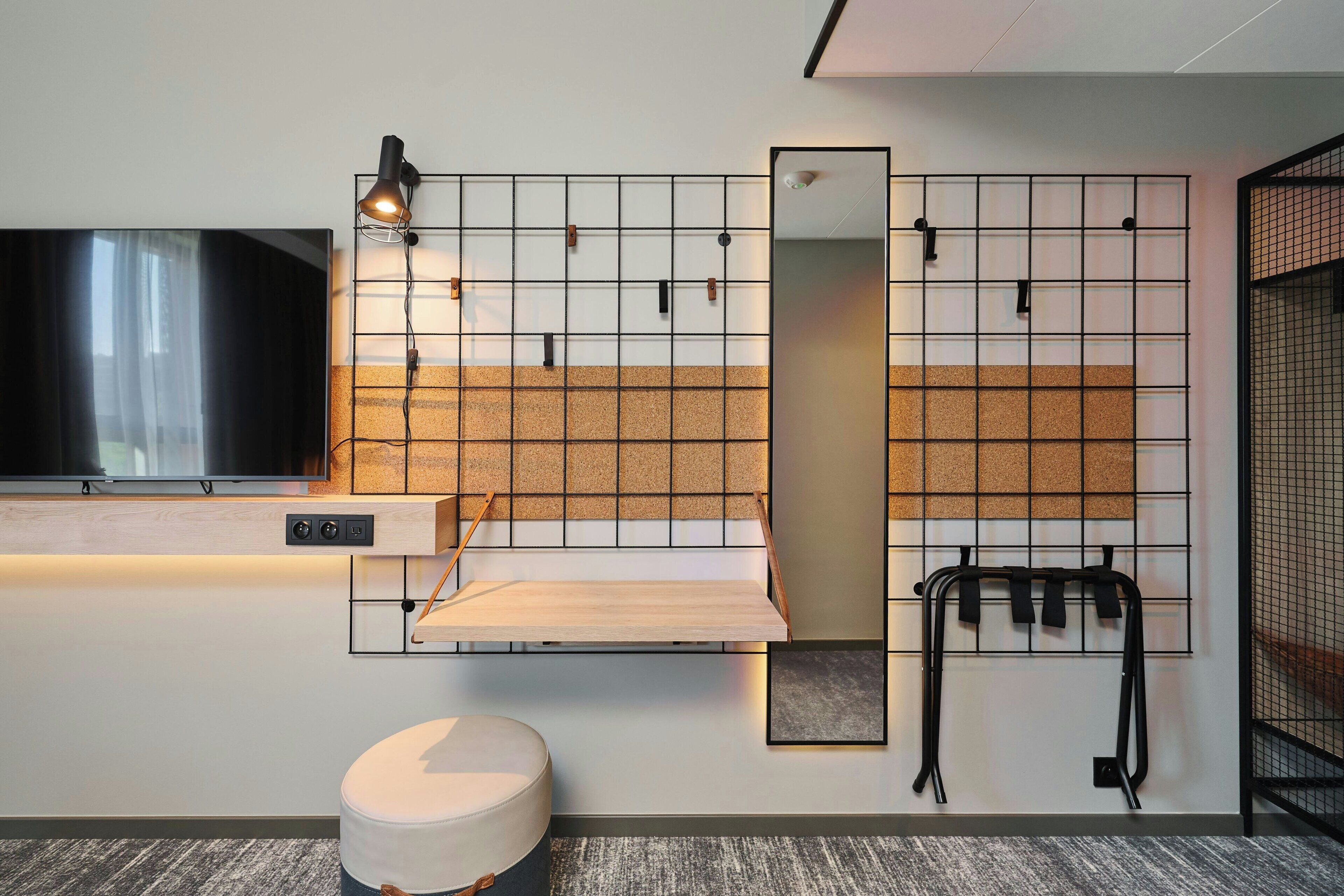Une chambre d’hôtel moderne équipée d’un téléviseur à écran plat, d’une étagère en bois, d’un miroir et d’un espace dédié à l’exercice physique.