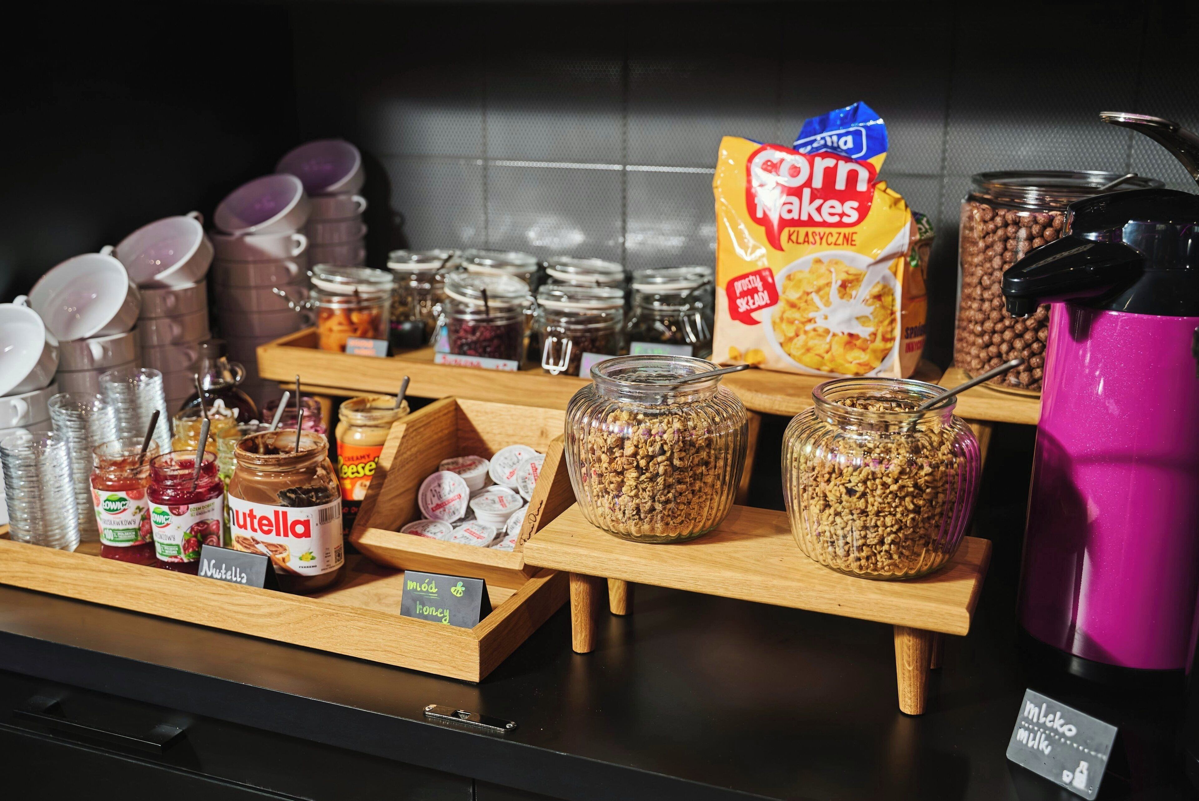 Aamiaistarjoilu, jossa on erilaisia ruoka-aineita, kuten purkkeja hilloa, Nutellaa ja mysliä.