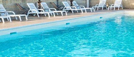 A swimming pool with white lounge chairs and a covered area with tables and umbrellas.