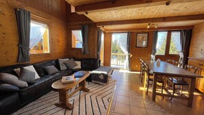 A wooden cabin interior with a black leather sofa, a wooden dining table, and a tiled floor. - Chalet soleil ski in ski out (La rosiere)