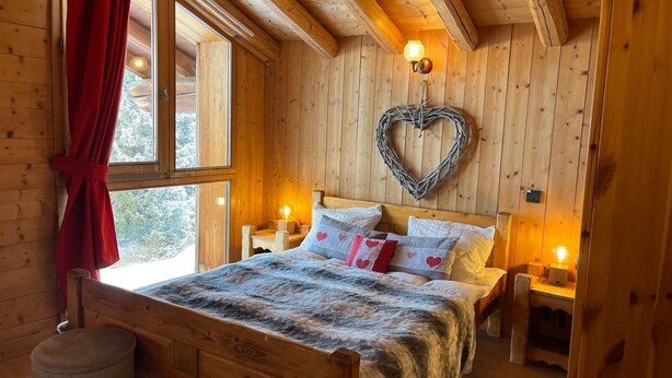 A cozy wooden cabin bedroom with a bed, heart-shaped wall decoration, and two bedside lamps. - Chalet soleil ski in ski out (La rosiere)