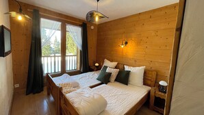 A wooden-paneled bedroom with a large bed, two bedside lamps, and a ceiling fan. - Chalet soleil ski in ski out (La rosiere)