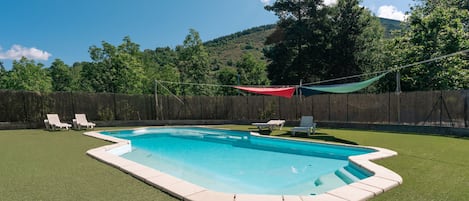 Una piscina con un área verde circundante, una valla de madera y montañas al fondo.
