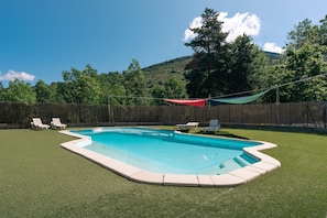 A swimming pool with a surrounding grassy area, a wooden fence, and a mountainous backdrop. - Le Sapin Cabin (Osséja)