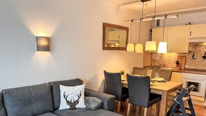 A modern living room with a grey sectional sofa, a dining table with chairs, and a kitchen area with cabinets and a stove. - Apartment Elwi by Interhome (Hahnenklee)