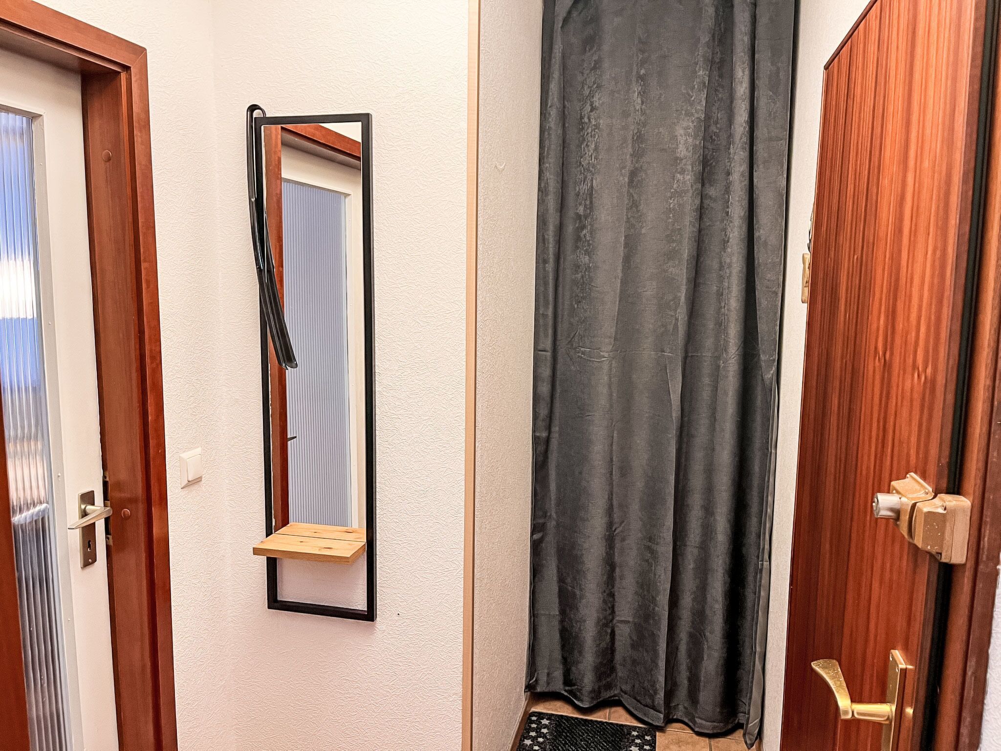 A bathroom with a wooden door, a mirror with a black frame, a towel rack, and a shower curtain.