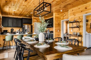 Un intérieur en bois avec une table à manger pour six personnes, des appareils de cuisine et un luminaire suspendu.