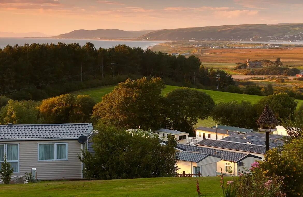 Área residencial com casas, um campo gramado e uma vista distante do mar e colinas.