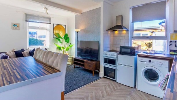 A compact living space with a dining area, a seating area with a TV, a kitchenette with a stove, oven, microwave, and washing machine.