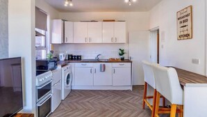 A compact kitchen with white cabinets, a built-in oven, a washing machine, and a dining area with a white table and chairs.