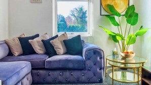 A living room with a purple sofa, a round glass coffee table, and a large green plant.