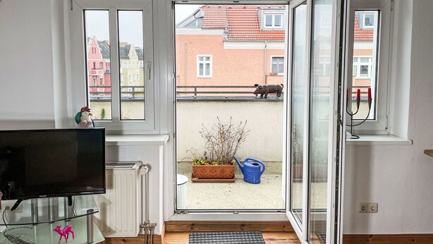 Une pièce avec une grande fenêtre, un radiateur, un téléviseur et une plante en pot.