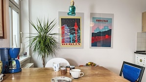 Un coin repas avec une table en bois, des chaises, une plante en pot et deux affiches au mur.