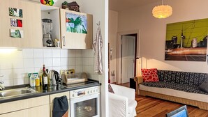 Une cuisine moderne équipée d’une cuisinière, d’un four et de divers appareils électroménagers. On y trouve également un coin repas avec un canapé et une table. La pièce est dotée d’un plancher en bois et d’une grande fenêtre.
