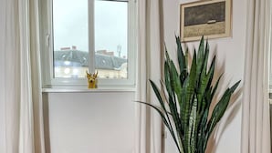 Une pièce avec une fenêtre, une plante en pot et un tableau encadré au mur.